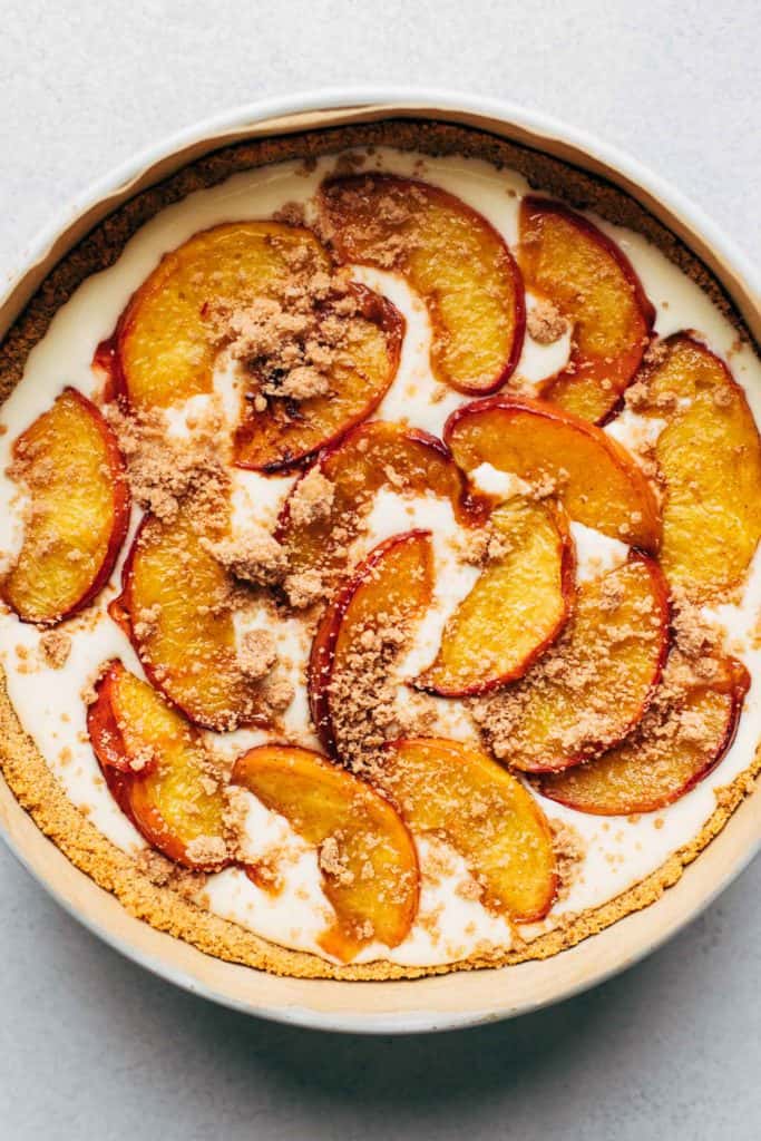 the top view of cheesecake batter half filled in a springform pan with roasted peaches laid on top